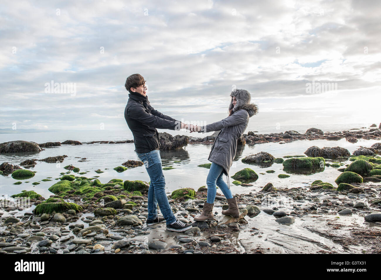 Ein junges Paar zu Fuß während halten die Hände am Strand von Porthmadog. Stockfoto