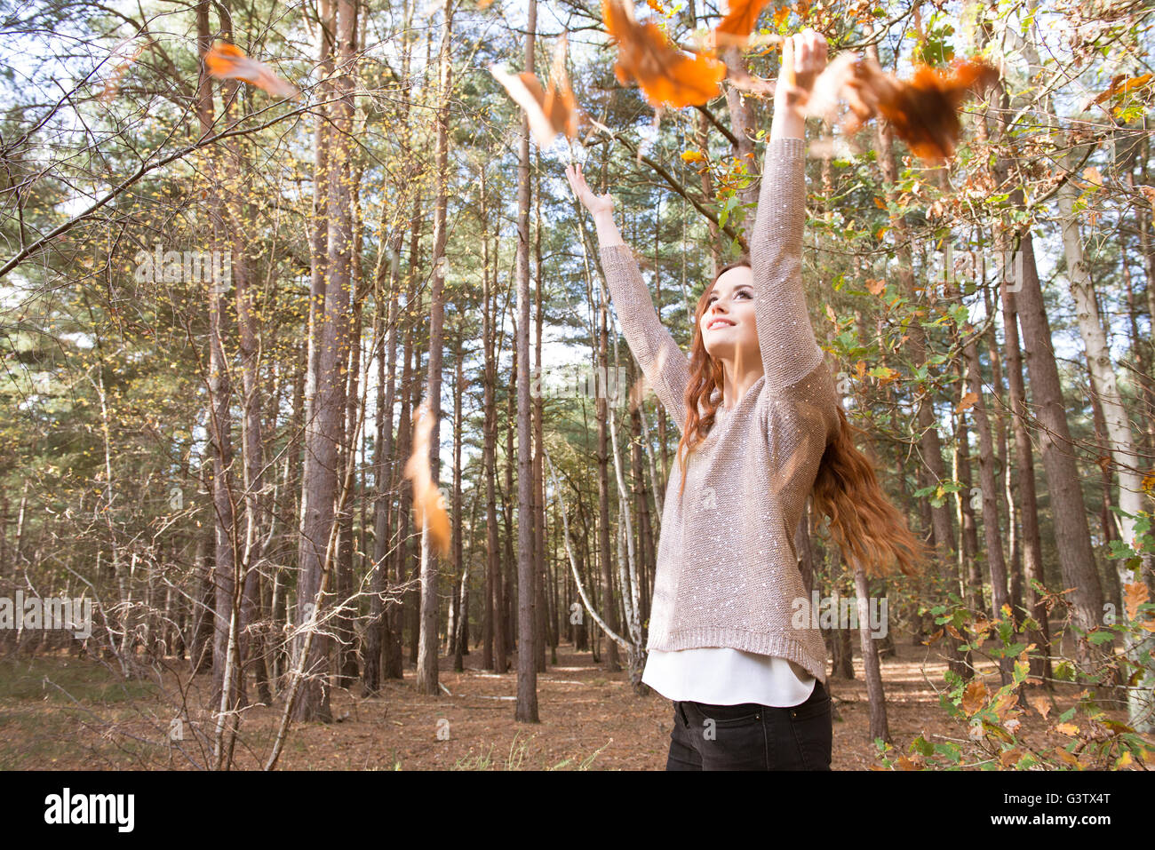 Eine junge Frau wirft eine Handvoll Blätter in einem Wald im Herbst. Stockfoto
