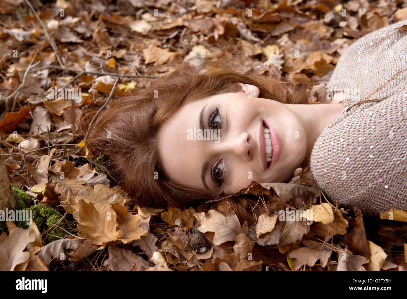 Eine attraktive junge Frau, die Verlegung auf dem Waldboden, umgeben von Blättern. Stockfoto