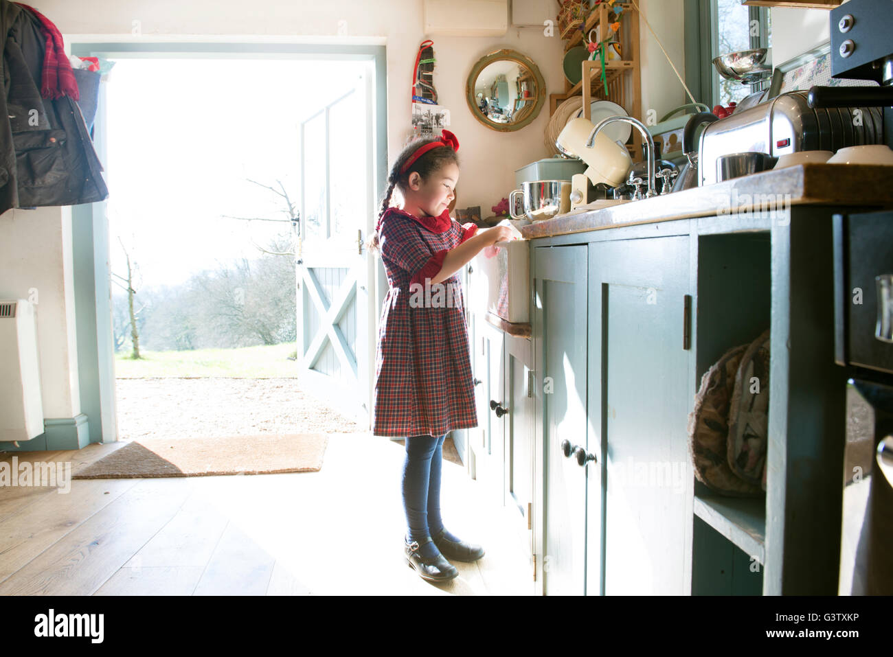 Ein sechs Jahre altes Mädchen beim Abwasch bei einer Küchenspüle. Stockfoto