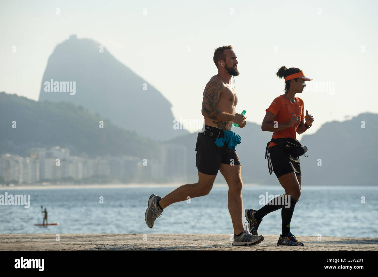 RIO DE JANEIRO - 3. April 2016: Ein paar Jogger auf dem Strand Straßenpass vor der Skyline der Stadt am Strand Copacabana. Stockfoto