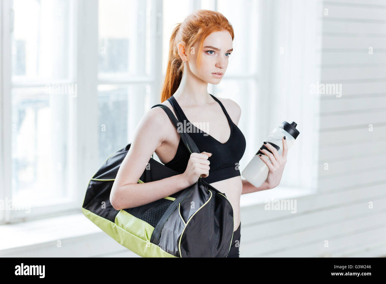 Junge hübsche Fitness Frau mit Sporttasche und Wasserflasche in der Turnhalle Stockfoto