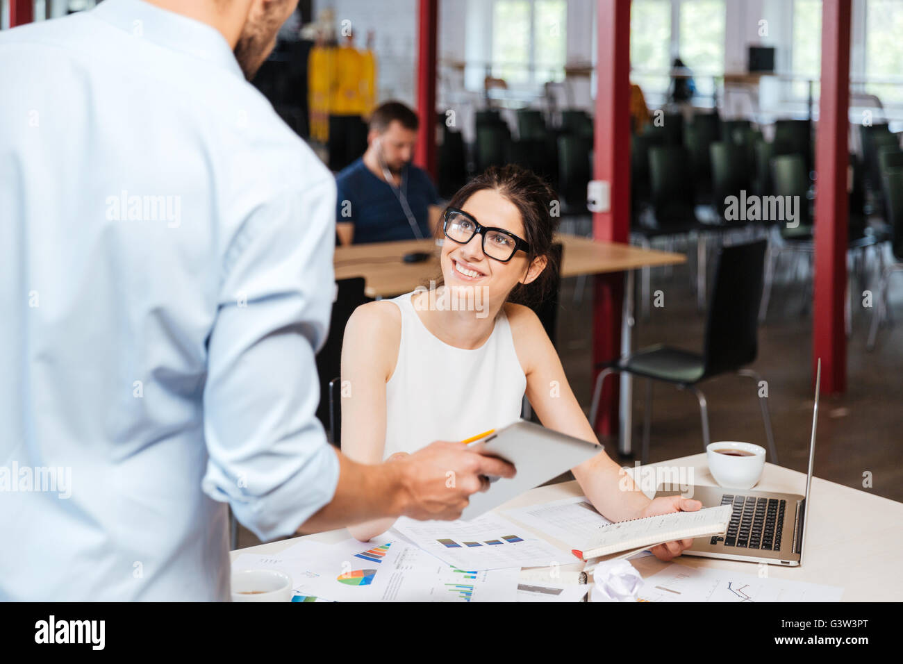 Fröhliche junge Geschäftsfrau in Glassses im Gespräch mit ihren Kollegen mit Tablet-PC im Büro Stockfoto