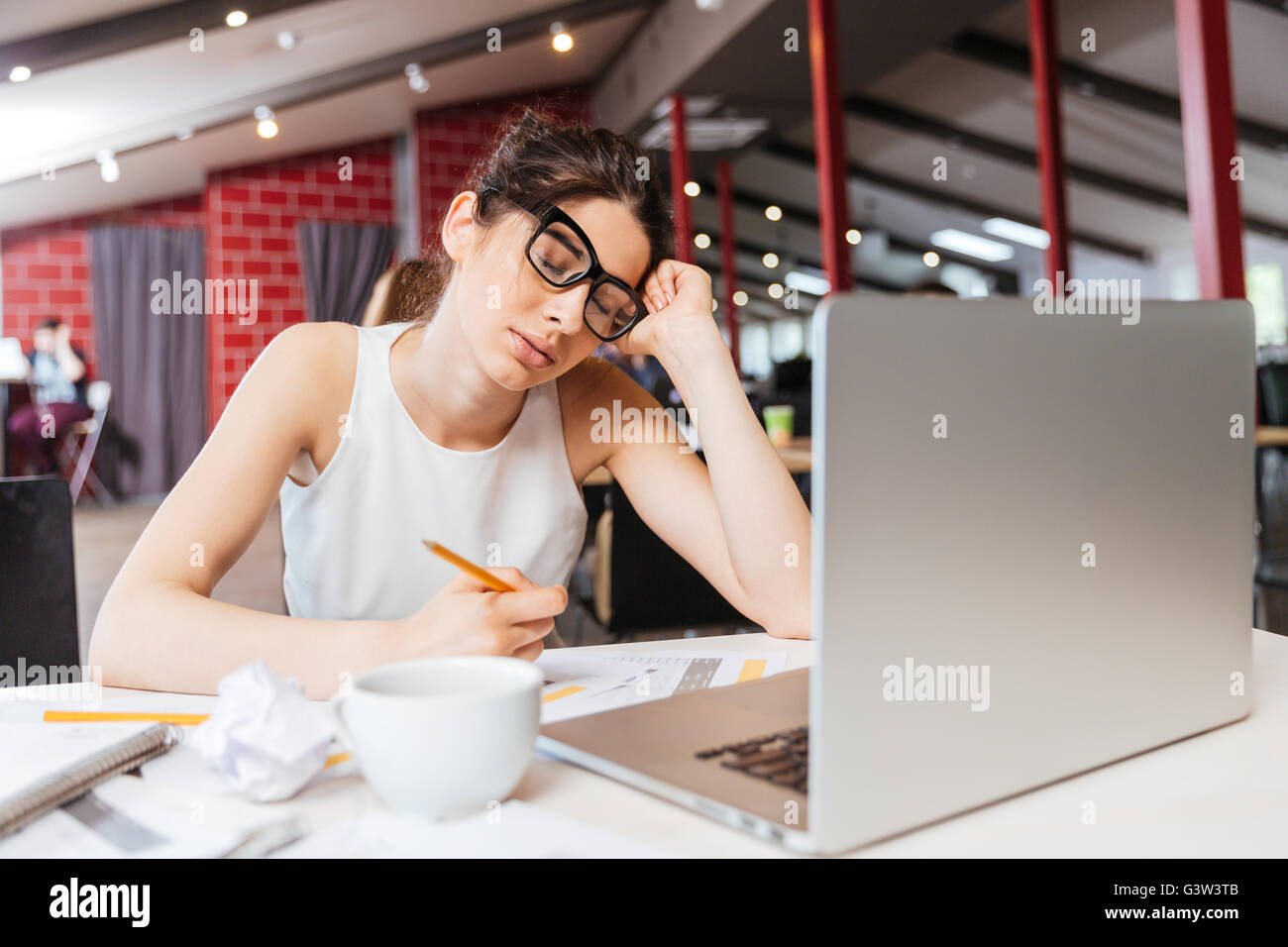 Müde, schläfrig junge Geschäftsfrau in Gläsern sitzen und arbeiten mit Laptop im Büro Stockfoto