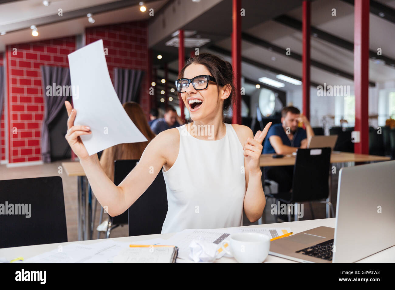 Lächelnde junge Frau in Gläsern zu arbeiten und Business-plan im Büro inspiriert Stockfoto
