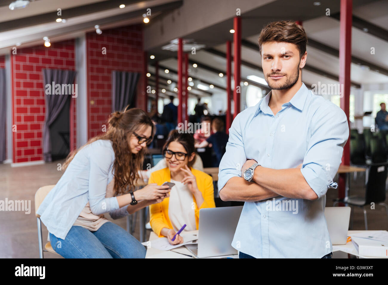 Sicher attraktive Jungunternehmer stehen mit verschränkten mit seinen Kollegen auf Hintergrund Stockfoto