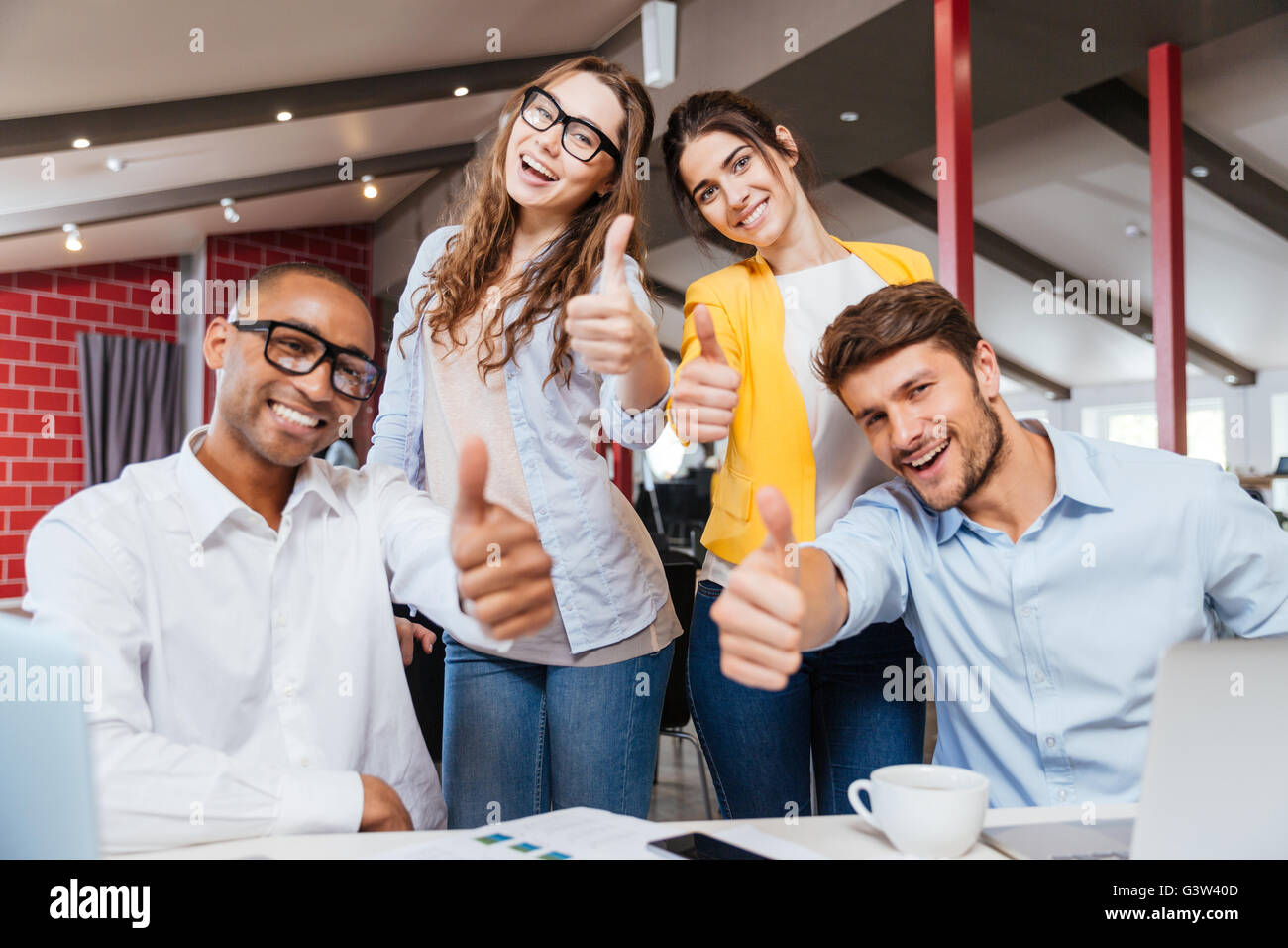 Lächelnd erfolgreiche junge Geschäftsleute zeigen, Daumen nach oben arbeiten im Büro Stockfoto