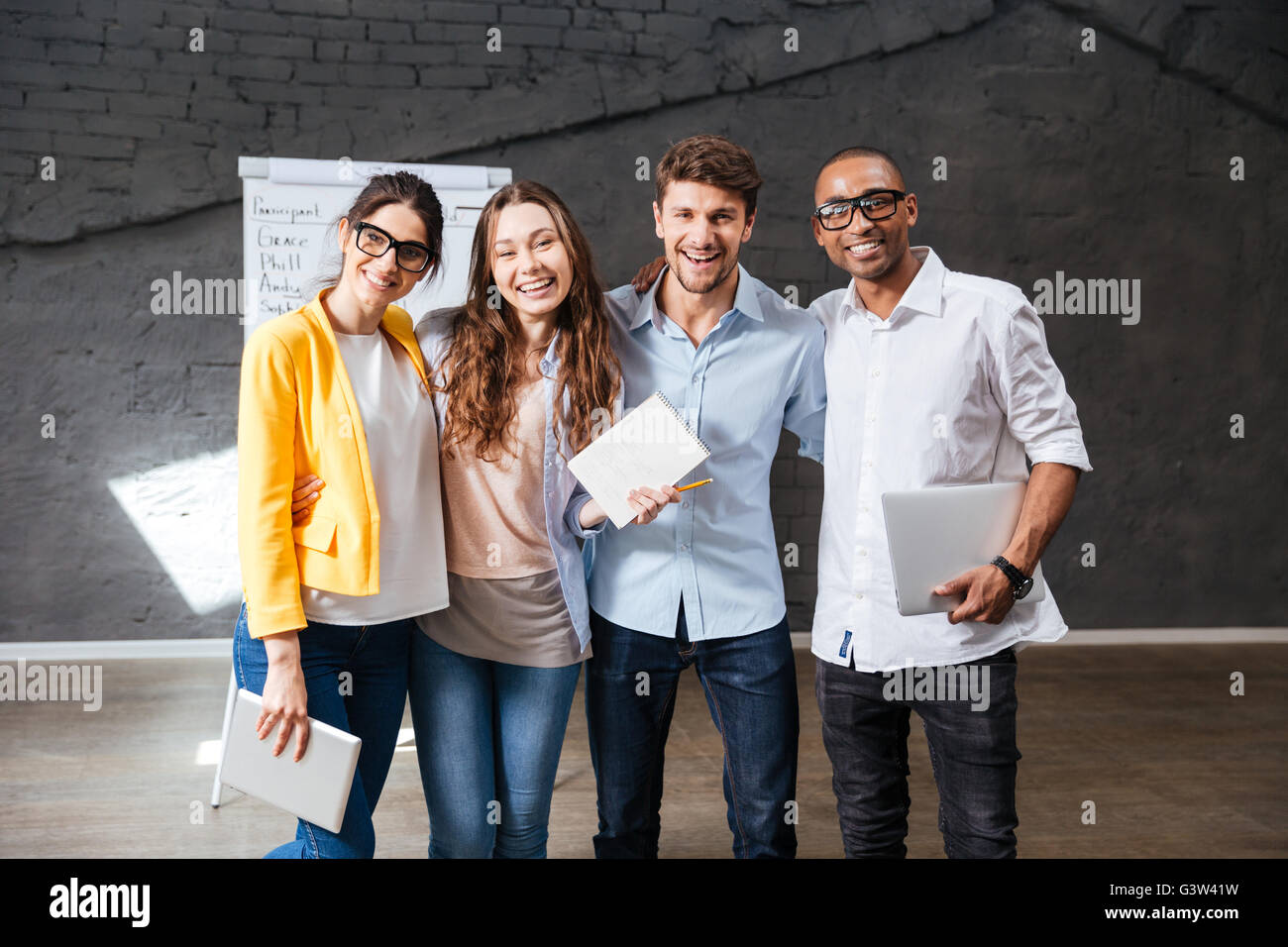 Multiethnische Gruppe der glückliche junge Geschäftsleute halten Tablet und Laptop stehen im Büro Stockfoto