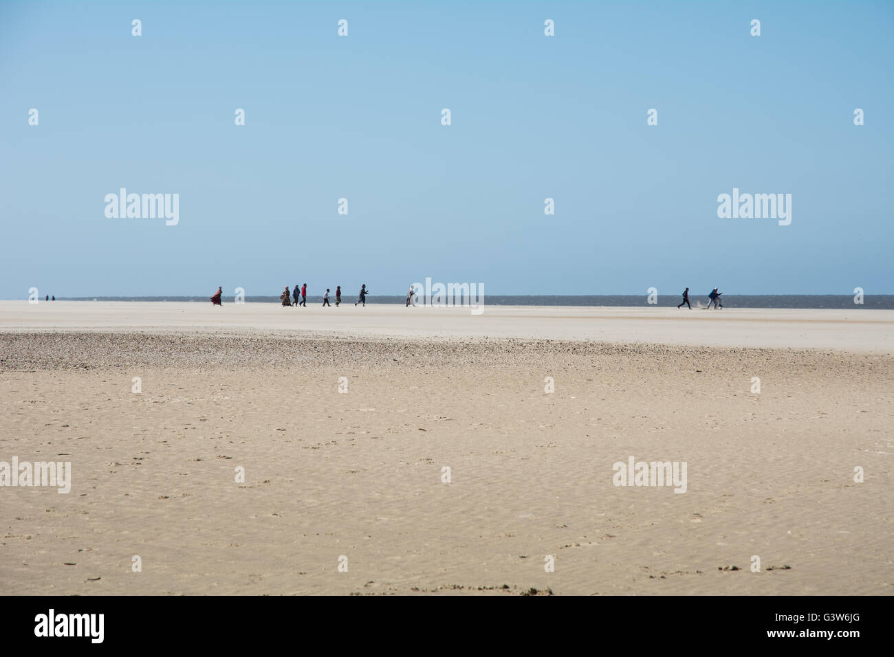 Eine Gruppe von Muslimen in traditioneller Kleidung am Strand entlang spazieren. Stockfoto