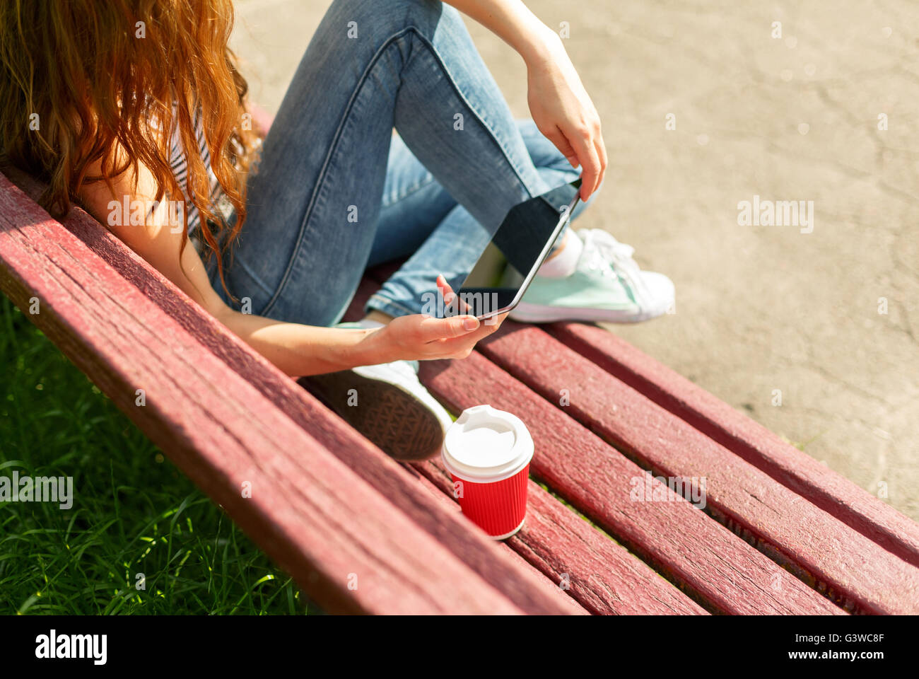 Junge Frau mit roten Einweg-Pappbecher Kaffee mit TabletPC sitzen auf einer roten Bank in einem park Stockfoto