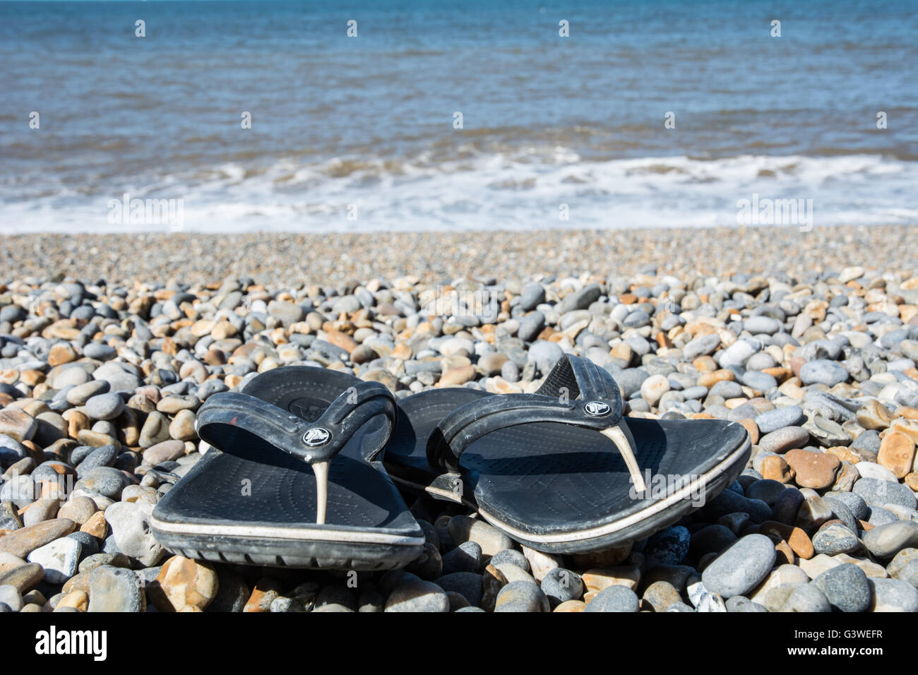 Ein paar Croc Flip-flops an einem steinigen Strand. Stockfoto