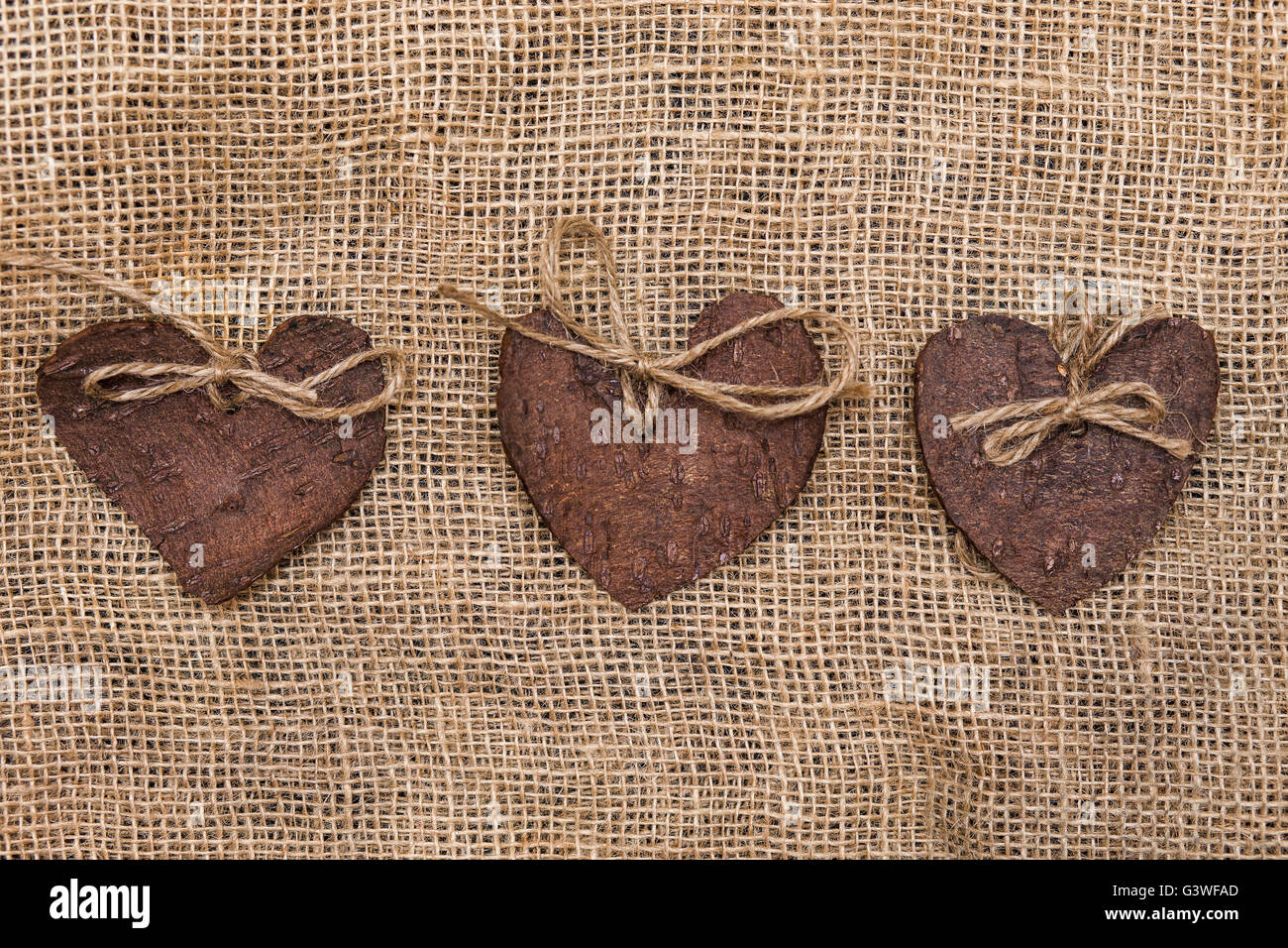 Drei 3 dekorative Herzen aus Baumrinde auf Sackleinen, Eco Dekor gefertigt. St. Valentinstag Grußkarte Idee. Handgefertigte Design. Stockfoto