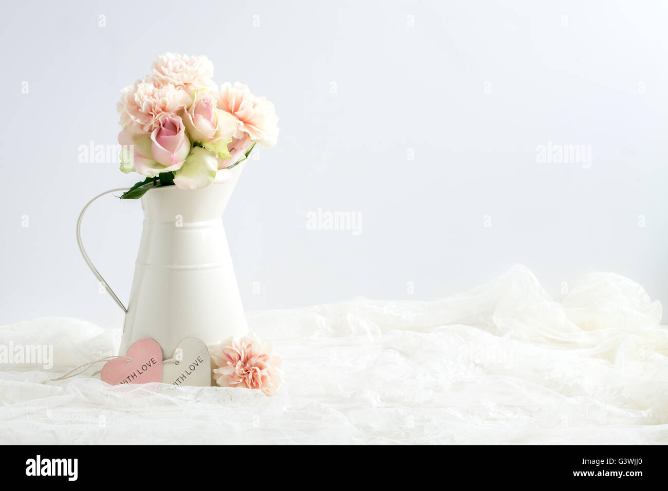 Mock-up stock Bild von Nelken, Rosen & Blüte in einem Sahnekännchen mit ein Stück Spitze gestylt. Stockfoto