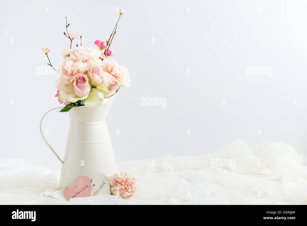 Mock-up stock Bild von Nelken, Rosen & Blüte in einem Sahnekännchen mit ein Stück Spitze gestylt. Stockfoto