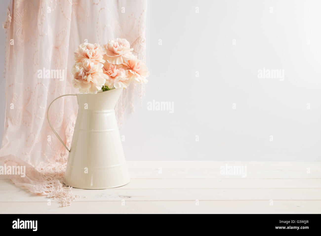 Mock-up gestylt stock Bild von Nelken in ein Sahnekännchen mit ein Stück Spitze hinter den Krug. Stockfoto