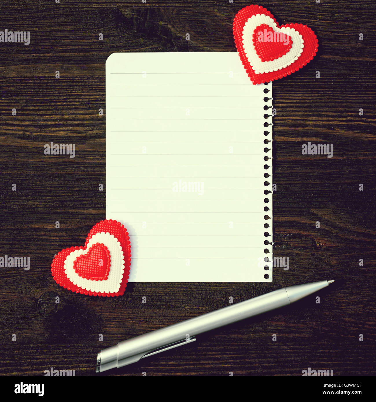 Ein leeres Blatt Papier, Stift und zwei Herzen auf einem hölzernen Hintergrund. Foto im Vintage-Stil Stockfoto