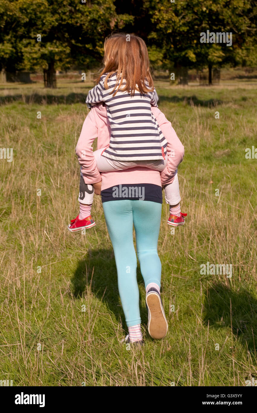 Immer eine Fahrt. Eine jüngere Schwester reitet auf dem Rücken ihrer älteren Schwester, wie sie für ein erforschen der weiten, offenen Flächen der Aufrechnung Stockfoto