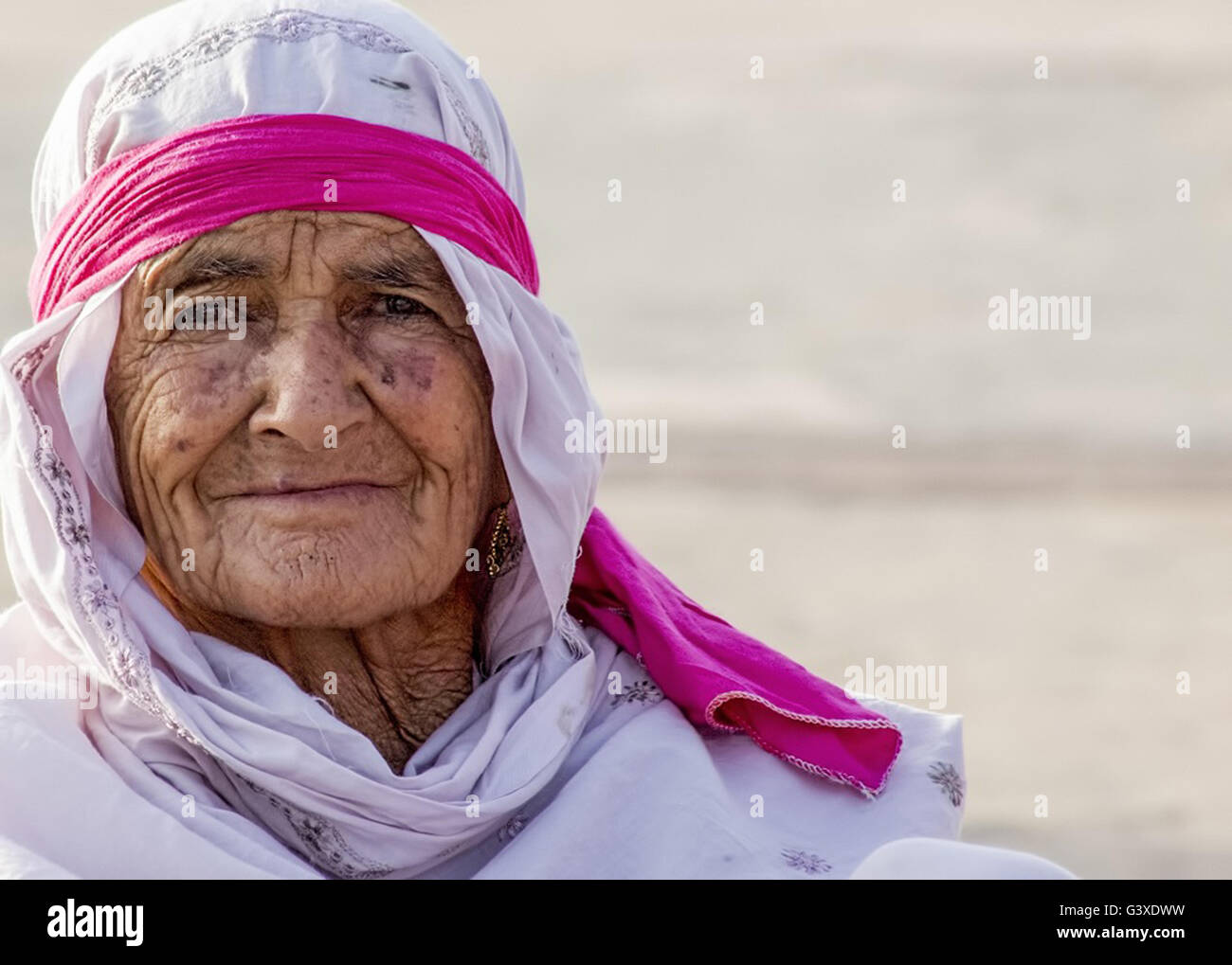 Ältere arabische Frau trägt ein weißes Gewand, Schal und roten Stirnband. Stockfoto