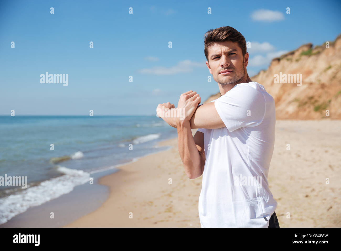 Überzeugt junge Sportler im weißen T-shirt Übungen am Strand Stockfoto