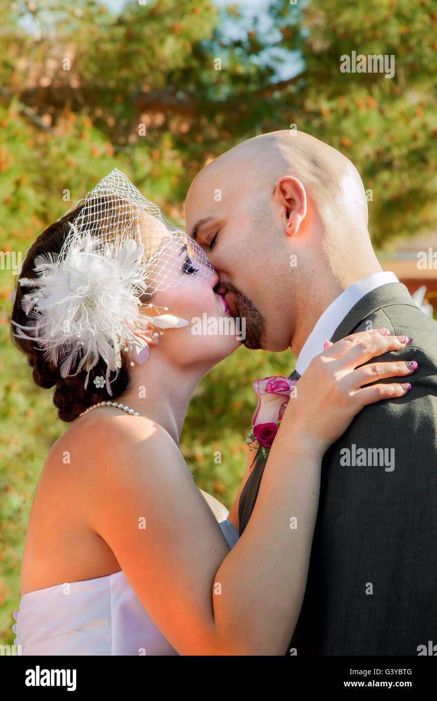 Eine Braut und Bräutigam während ihrem ersten Kuss als verheiratetes Paar.  Die Braut trägt einen Vogelkäfig Schleier. Stockfoto