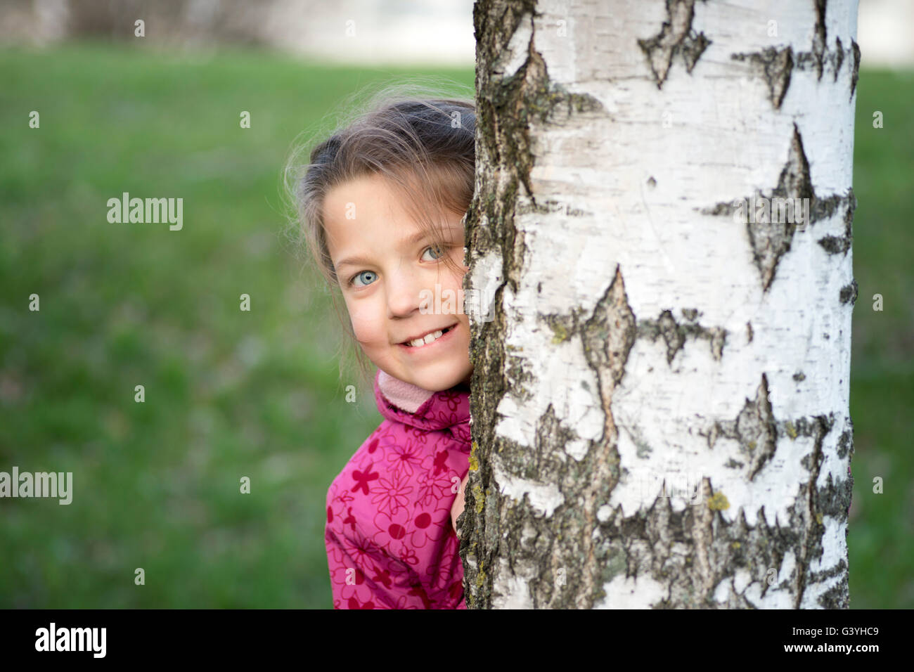 fröhliches Mädchen versteckt sich hinter Birke Stamm bis zum Frühjahr Stockfoto