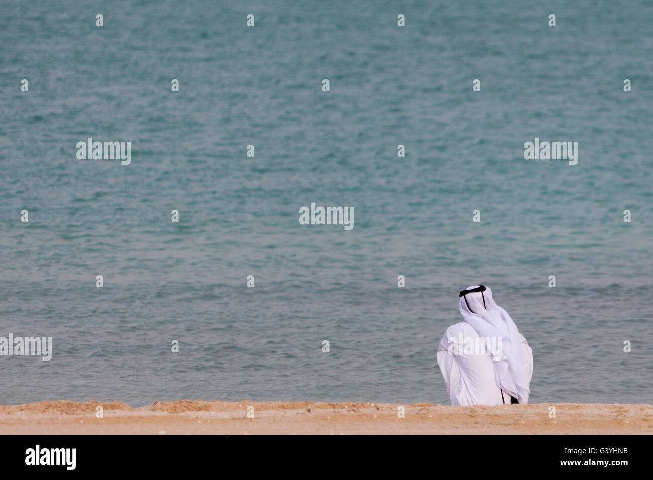 Arabische Mann in traditioneller Kleidung, sitzen am Strand mit Blick auf das Meer Stockfoto