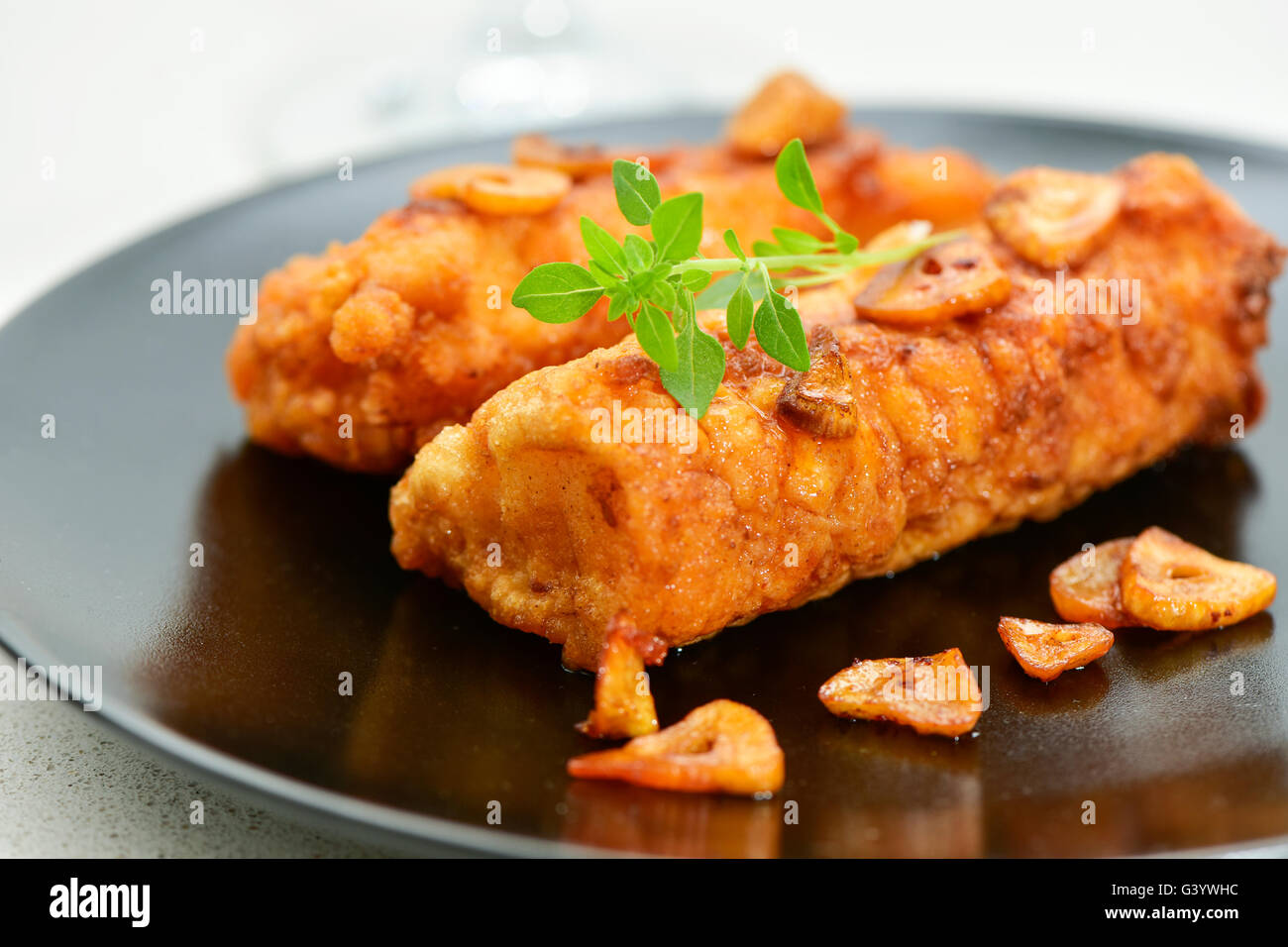 Nahaufnahme von einigen geschlagen und gebratenen Kabeljau Filets mit gebratenem Knoblauch, serviert in einer schwarzen Platte bedeckt Stockfoto