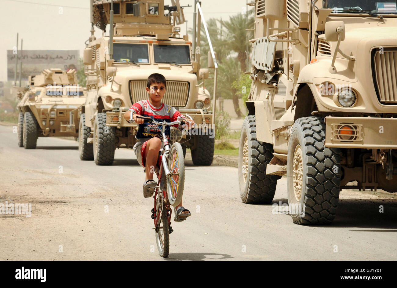 Eine irakische junge fährt Rad vorbei an einer US-Militär Fahrzeug-Patrouille. Stockfoto