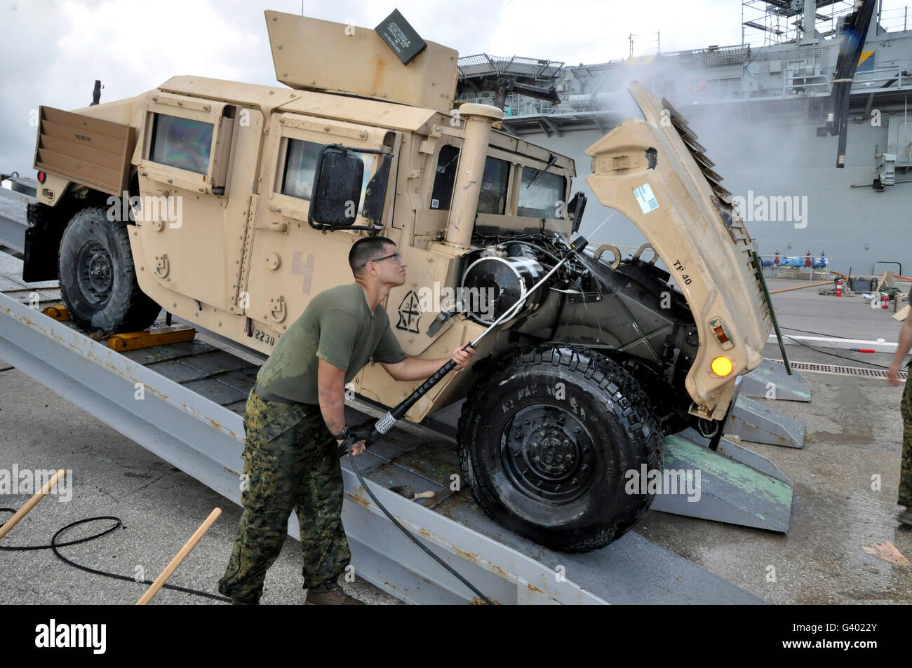 Marine nutzt einen Hochdruckreiniger um zu reinigen Sie die Unterseite der Haube ein Humvee. Stockfoto