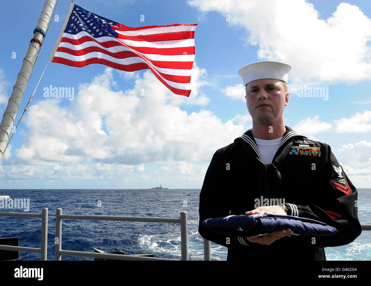 Ein Seemann trägt der nationalen Fähnrich während einer Beerdigung am Meer Zeremonie. Stockfoto
