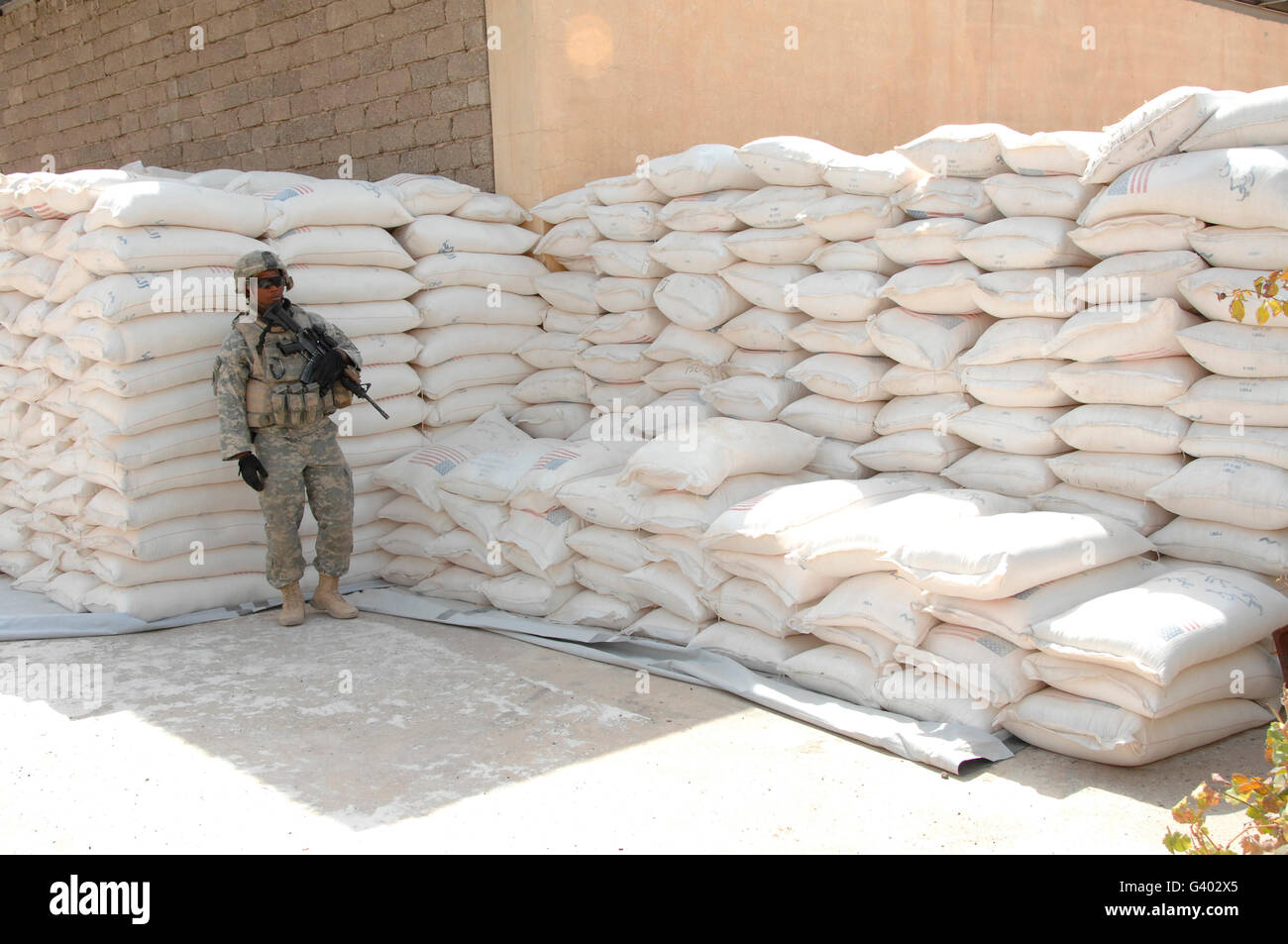 Ein US-Soldat sorgt für Sicherheit im Schatten von einem Berg von Mehl Beuteln. Stockfoto