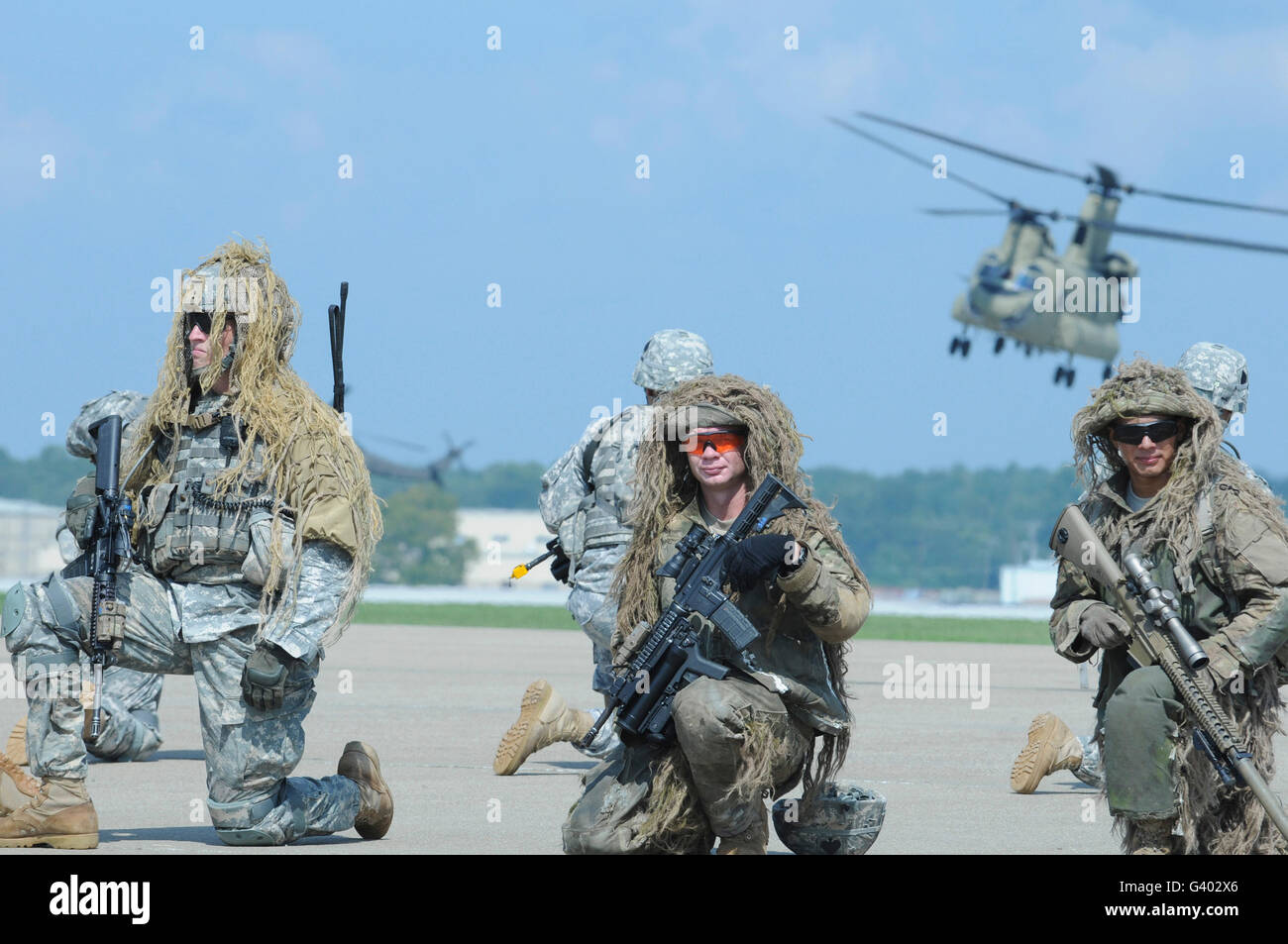 Soldaten in Ghillie-Anzügen zu nehmen eine Knie wie ein CH-47 Chinook über Kopf fliegt Stockfoto