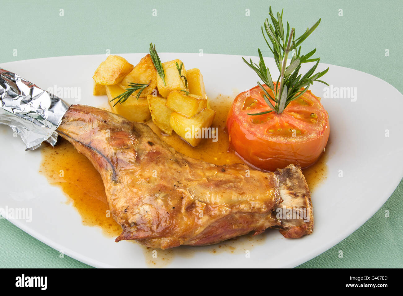 Bein von Milchlamm mit gerösteten Tomaten und Pommes frites Stockfoto
