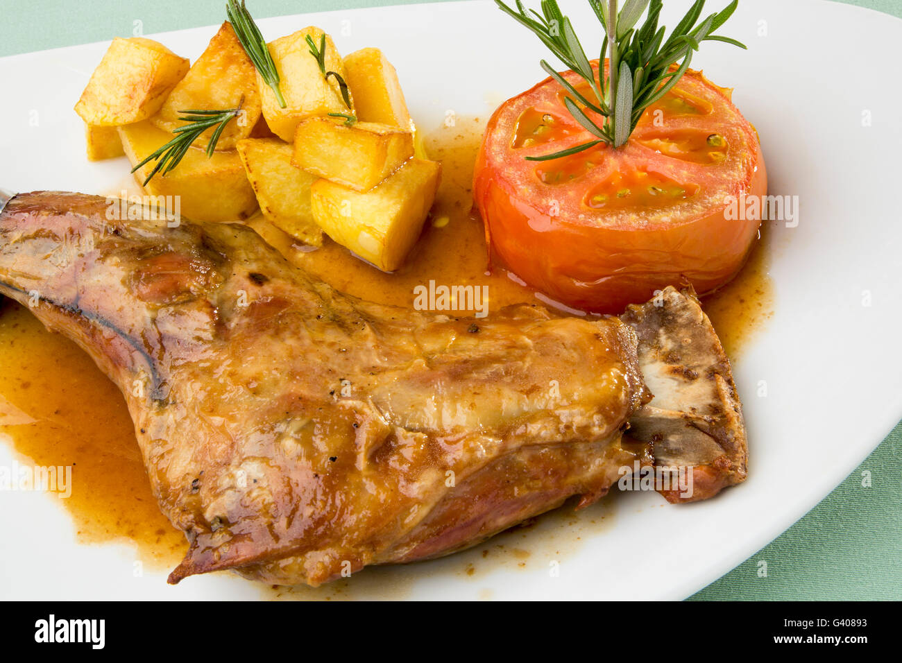 Bein von Milchlamm mit gerösteten Tomaten und Pommes frites Stockfoto
