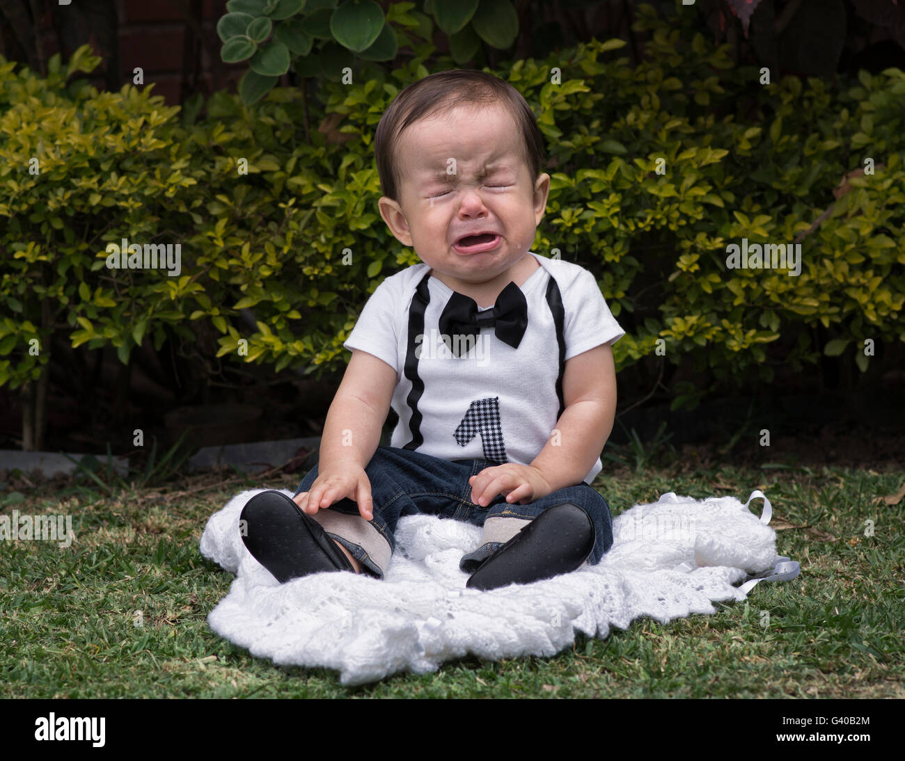 Einjährigen Baby Junge sitzt in einem Garten Weinen Stockfoto
