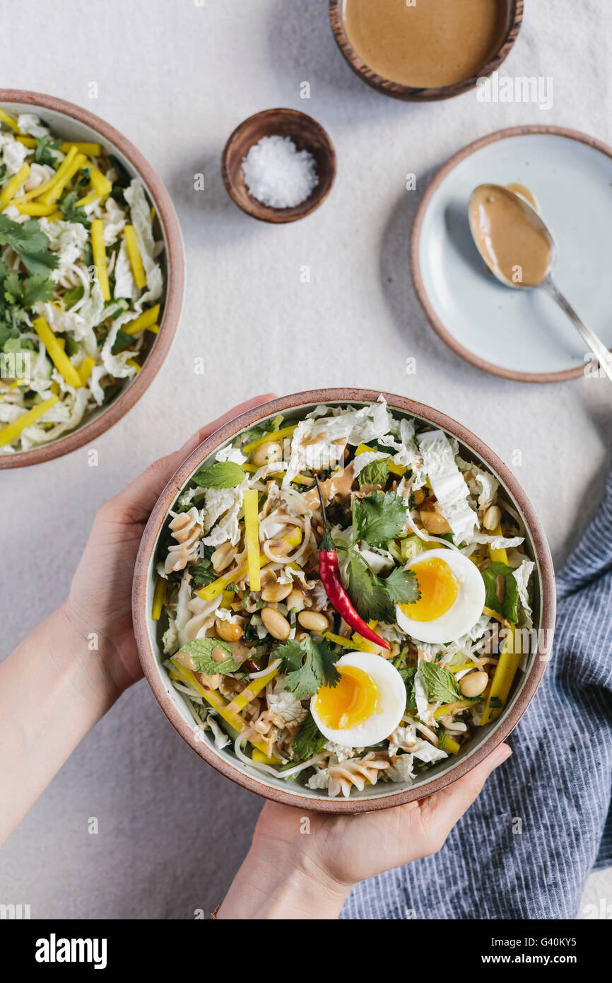 Eine Frau ist eine Schüssel mit knackigen Veggie Schüssel mit warmen Erdnuss Dressing auf dem Tisch platzieren. Stockfoto