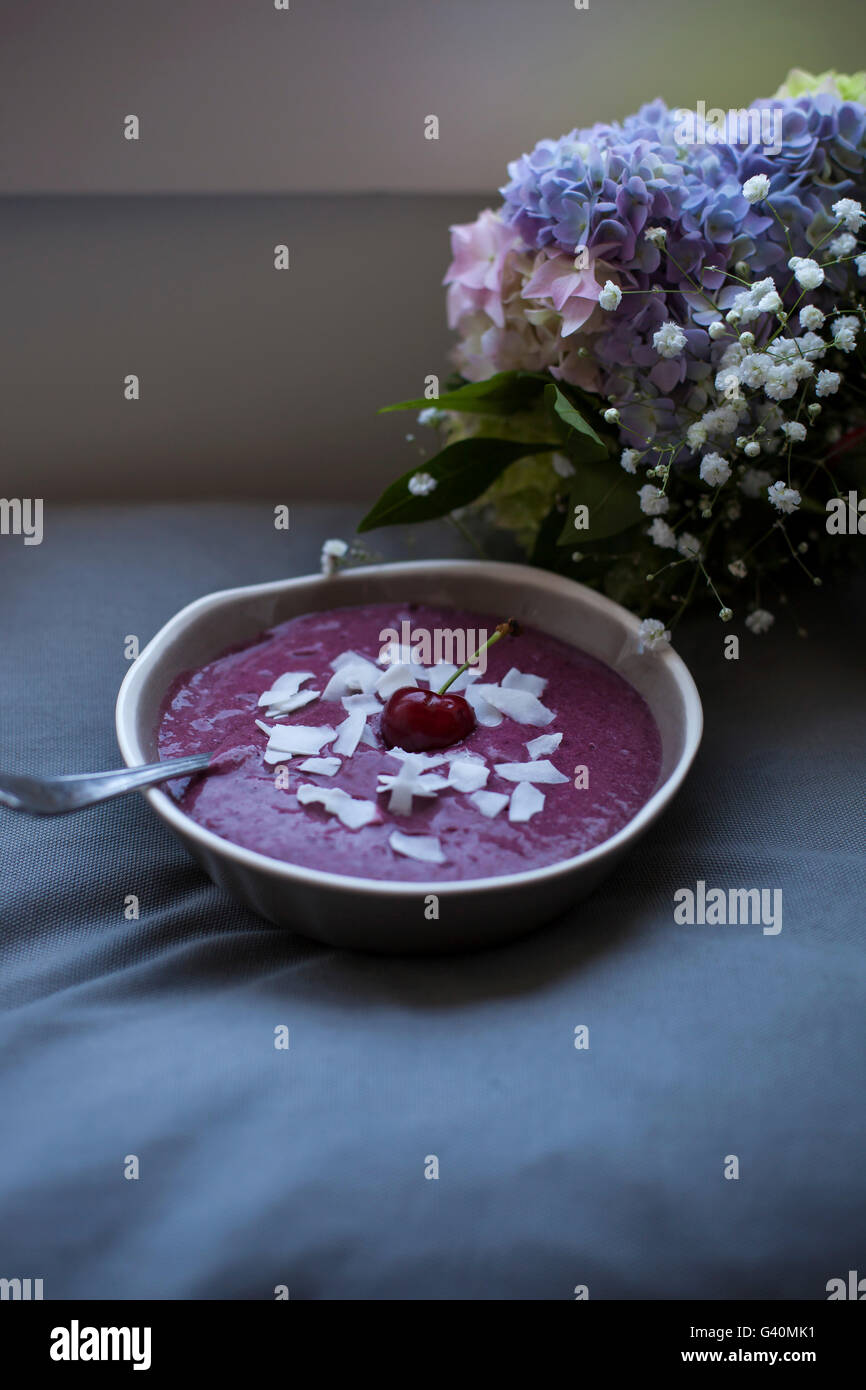 Kirsche Kokos Smoothie in eine graue Schale, garniert mit Kokosflocken und eine ganze Kirsche Stockfoto