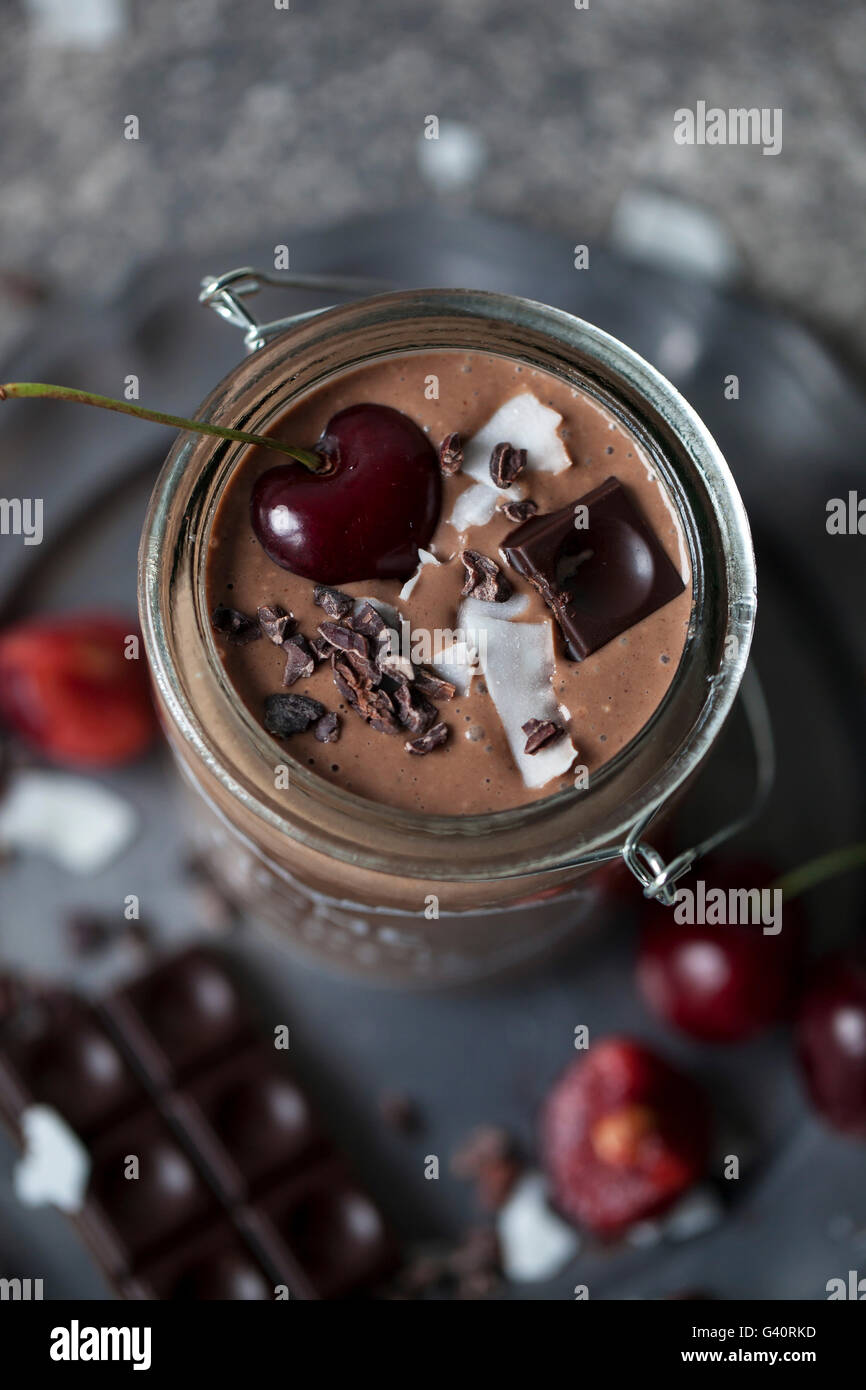 Schokolade Kokos Smoothie in einem Glas, garniert mit Kirschen, dunkle Schokolade, Kokosflocken und Kakaonibs Stockfoto
