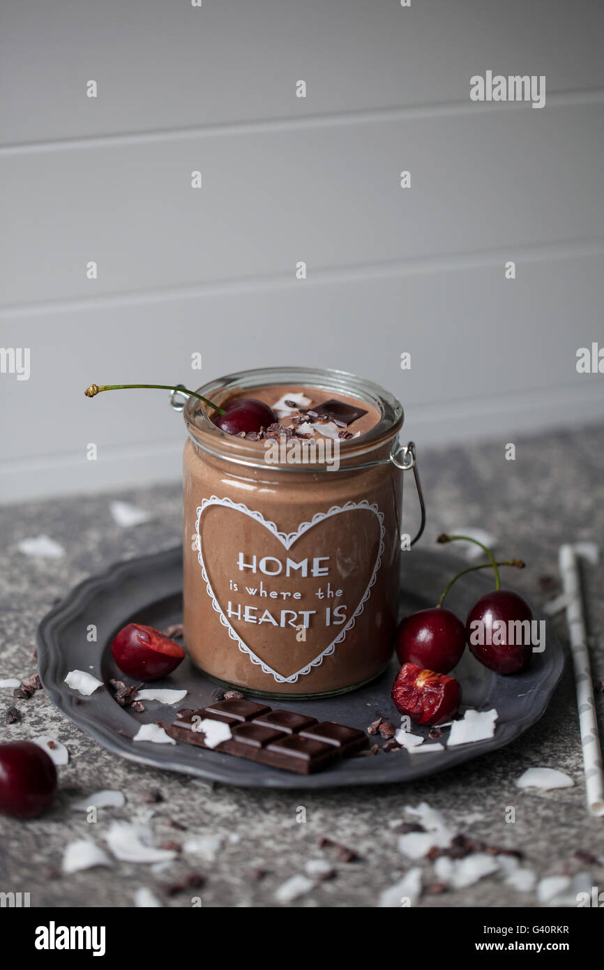Schokolade Kokos Smoothie in einem Glas, garniert mit Kirschen, dunkle Schokolade, Kokosflocken und Kakaonibs Stockfoto
