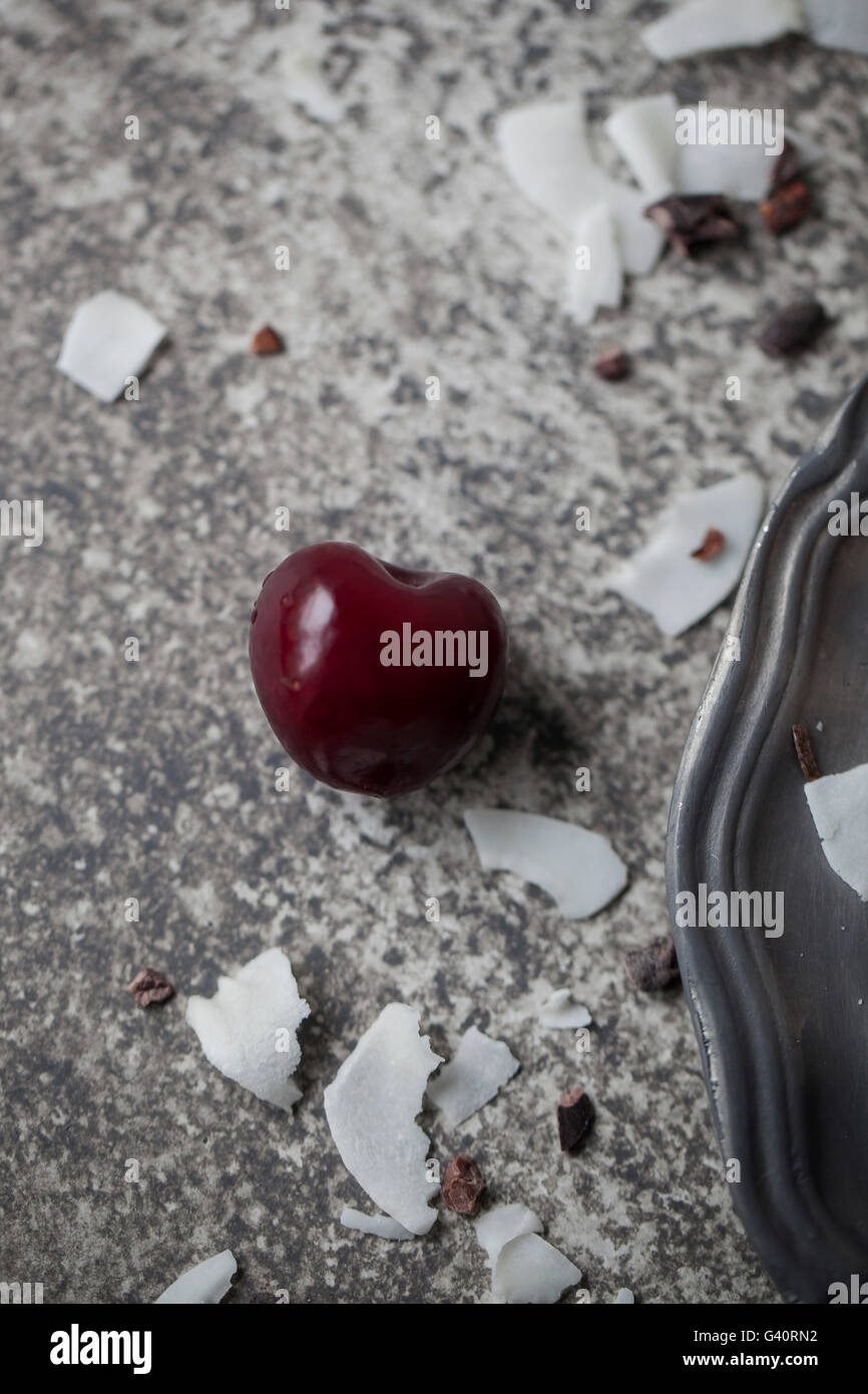 Einzelne Kirsche und Kokosnuss Flocken auf grauem Hintergrund Stockfoto