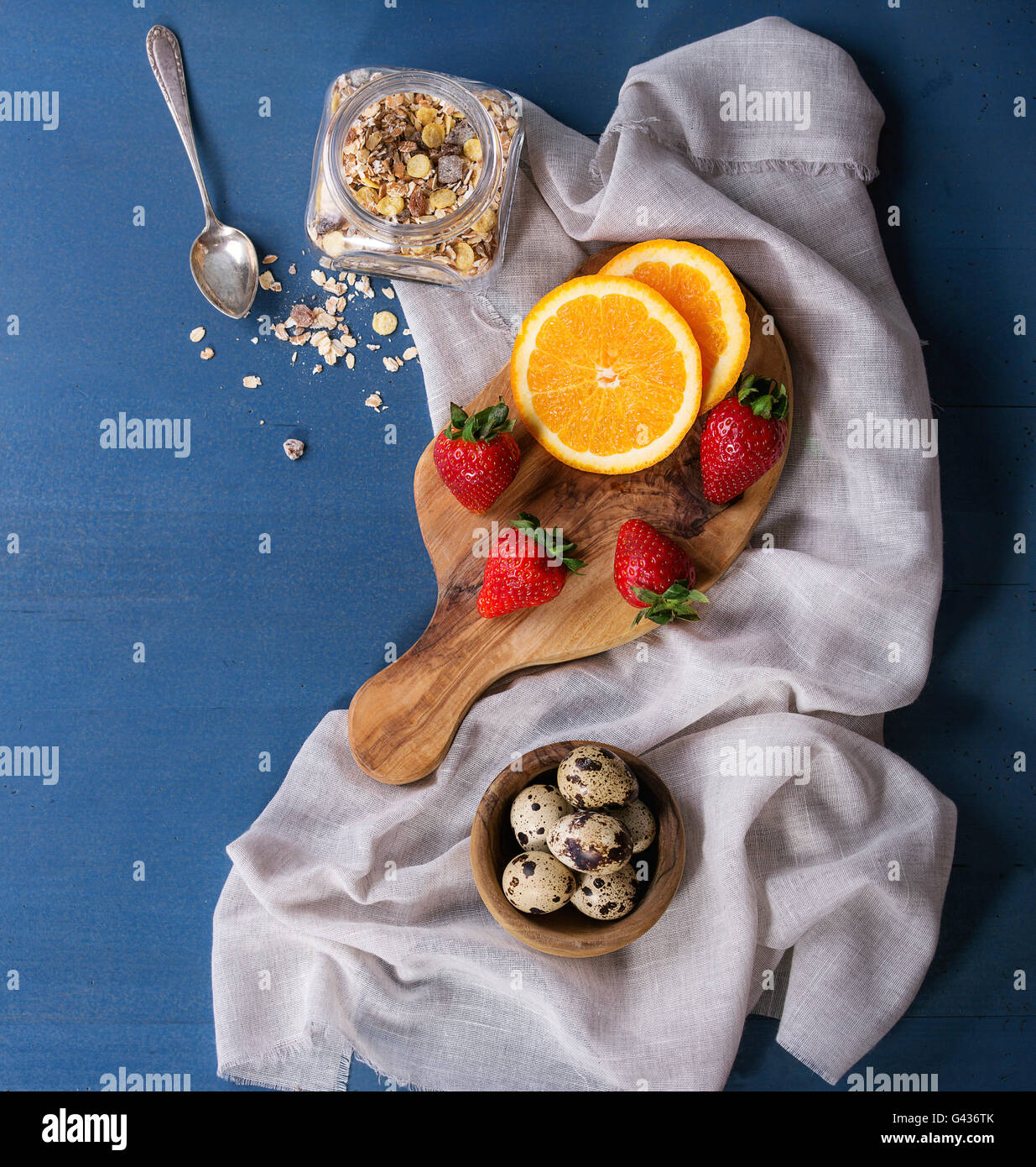 Zutaten für gesundes Frühstück. Wachteleier, Glas von Müsli, frische Orangen und Erdbeeren auf Olivenholz Schneidebrett mit te Stockfoto