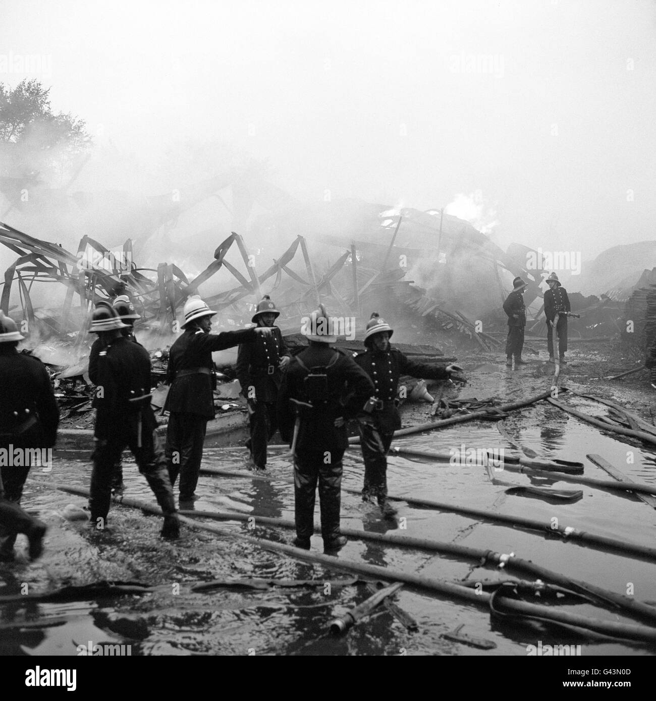 Feuerwehrarbeit unter den noch immer rauchenden Trümmern am Schauplatz eines massiven Feuers auf einem großen Holzhof in Tottenham im Norden Londons. Zweihundert Feuerwehrmäner und 50 Geräte kämpften gegen den Brand. Stockfoto