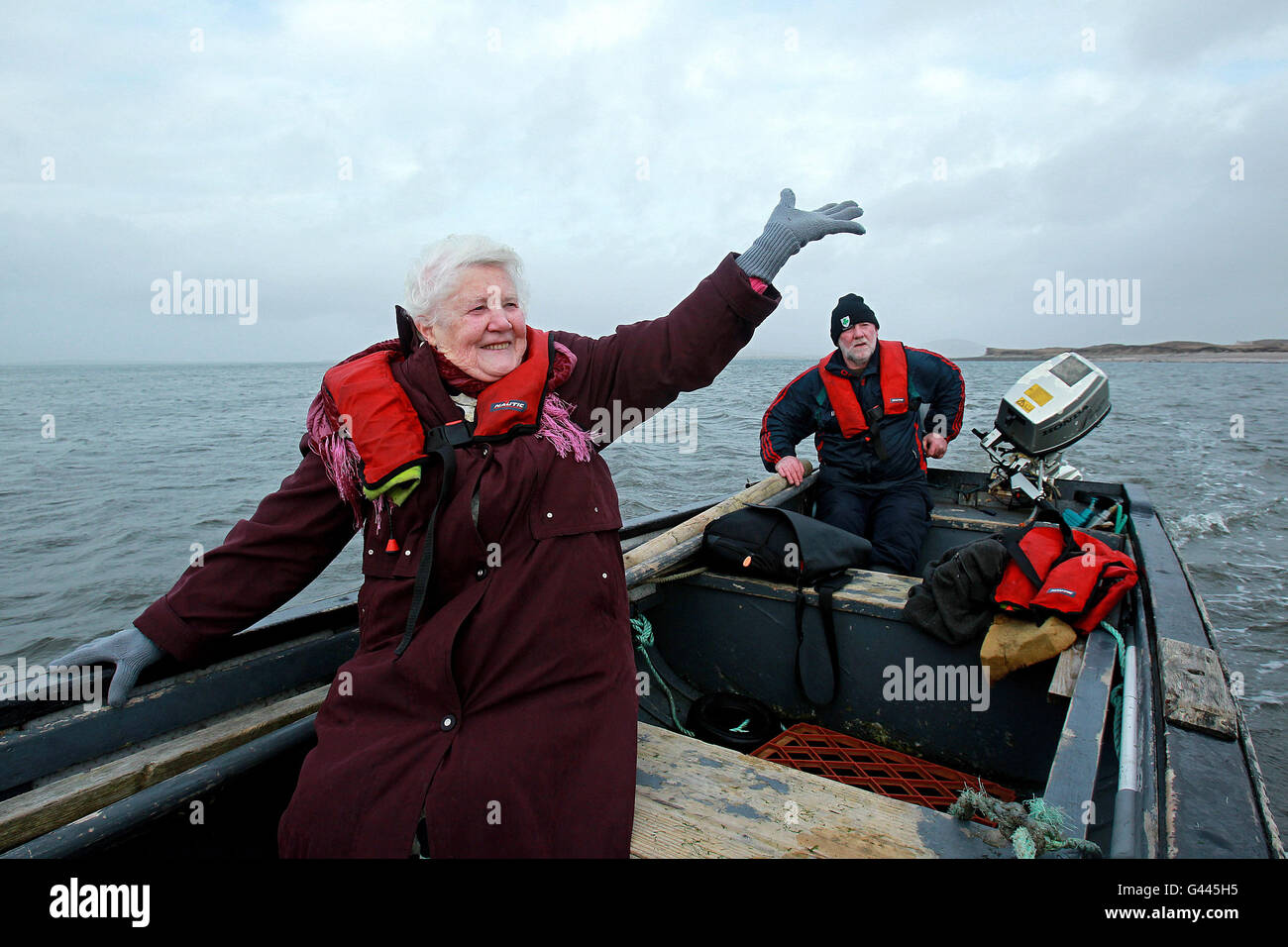 Islander Bridgie O'Malley, 83, winkt Auf Wiedersehen auf Inishbiggle zu ihren Freunden, als sie mit ihrem Sohn Joe O'Malley auf dem kleinen Boot nach Hause nach Achill zurückkehrt, nachdem sie bei den irischen Parlamentswahlen 2011 ihre Stimme abgegeben hatte. Sie stimmte im Wahllokal im alten Schulhaus von Spoil Mhuire auf Inishbiggle (Inis Bigil auf Irisch), einer kleinen bewohnten Insel vor der Küste der Grafschaft Mayo in Irland. Sein Name auf Irisch bedeutet "Insel des Fastens und hat nur 24 registrierte Wähler. Stockfoto