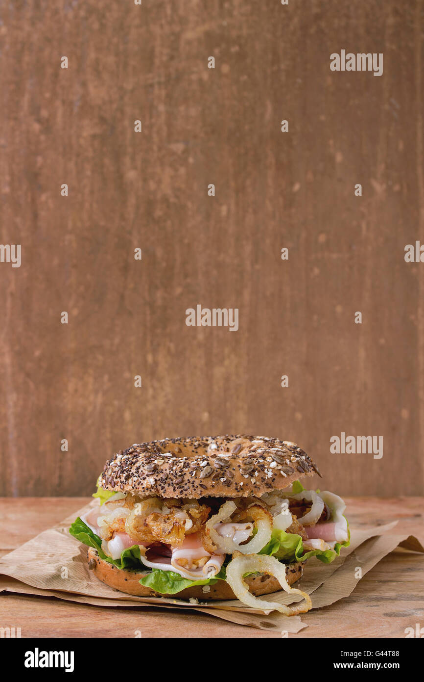 Ganze Korn Bagel mit gebratenen Zwiebeln, grüner Salat und Schinken Schinken auf dem Papier über Holz strukturierten Hintergrund. Mit Textfreiraum Stockfoto