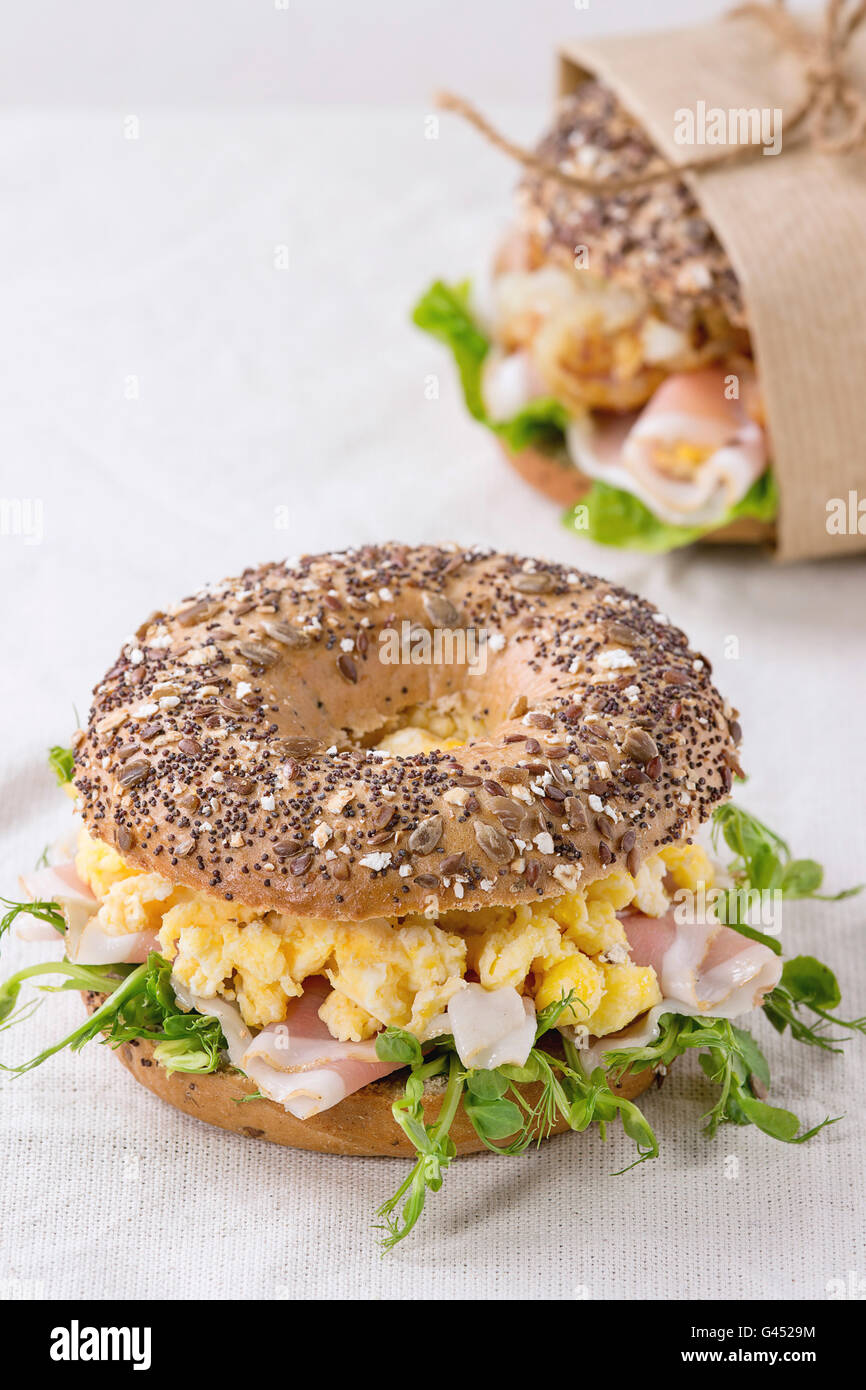 Ganze Korn Bagels mit Rührei, Erbse sprießen und Prosciutto-Schinken auf Holzplatte über hölzerne strukturierten Hintergrund. Stockfoto