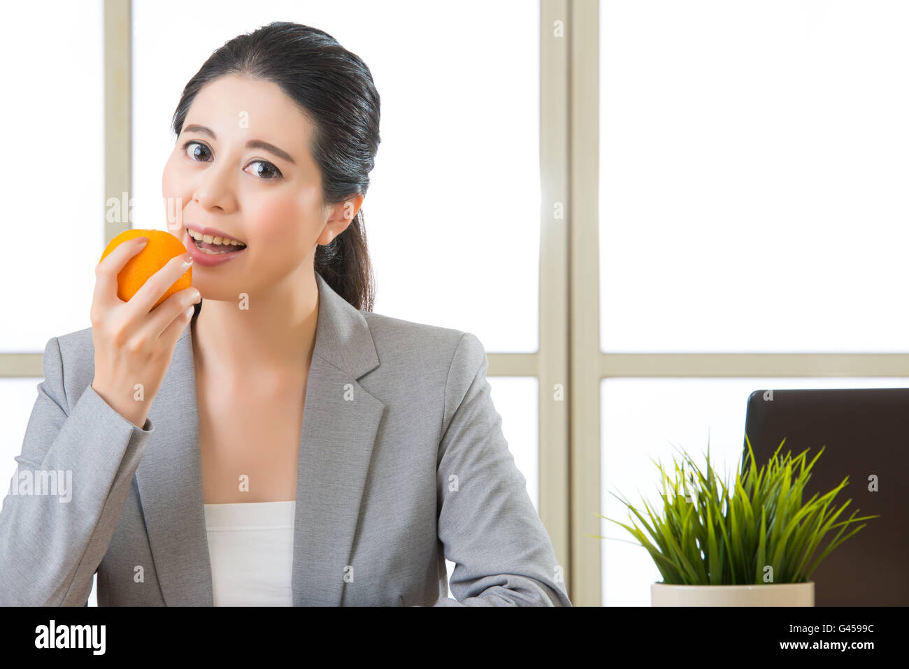 Junge asiatische Geschäftsfrau essen gesunde Snack orange im Büro Stockfoto