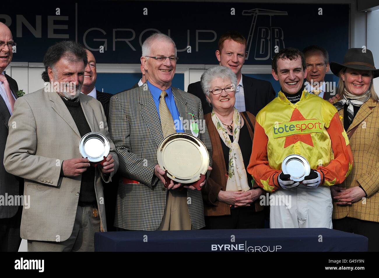 Holmwood Legend Trainer Pat Rodford (links), Besitzer Brian Derrick (Mitte) und Jockey Kieran Burke (dritte rechts) erhalten ihre Trophäen nach dem Sieg in der Byrne Group Plate (Grade 3 Handicap Chase) am St. Patrick's Day, während des Cheltenham Festivals Stockfoto