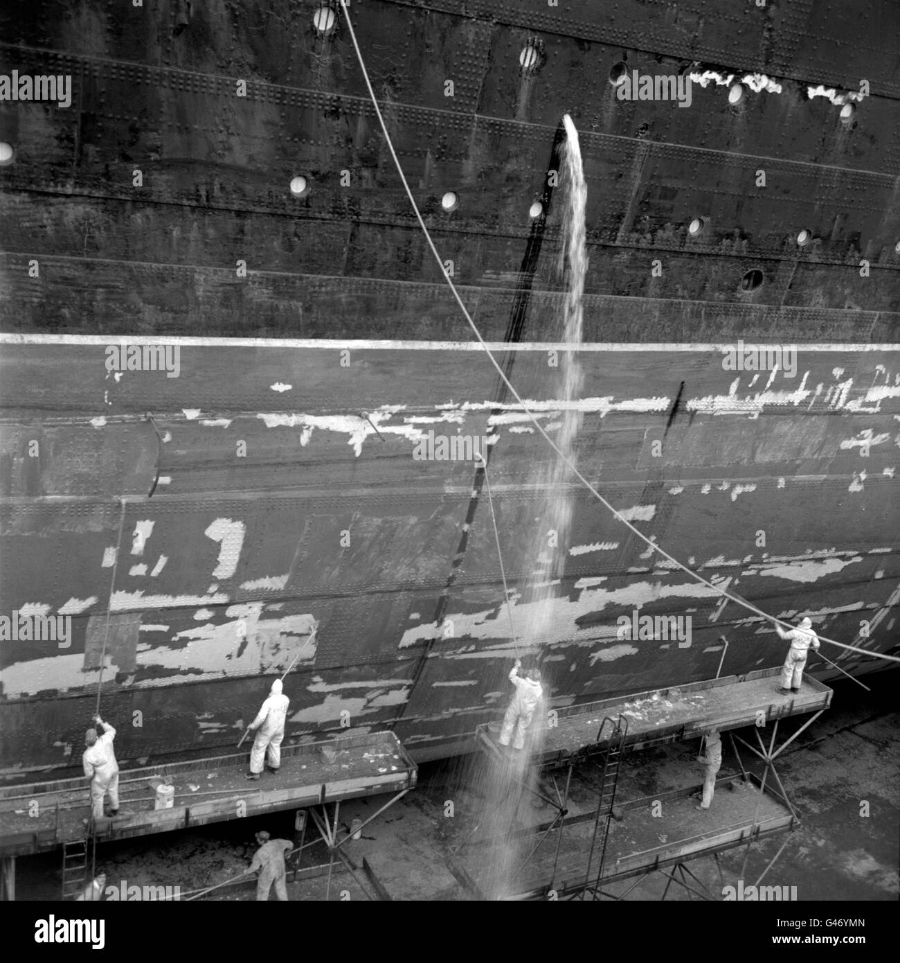 Eine Flut von Wasser kommt zu einem Arbeiter, der am Rumpf des Liners „RMS Queen Elizabeth“ im King George V Dry Dock in Southampton arbeitete. Stockfoto