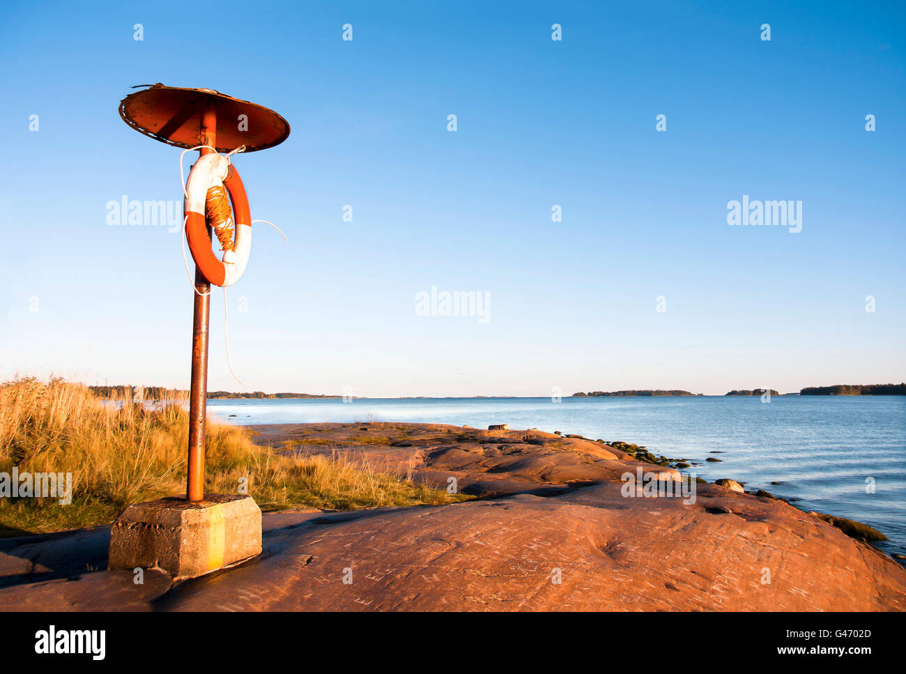 Rettungsring hängen an einen Pfosten auf felsigen Küste in der Nähe von Meer bei Sonnenuntergang im Sommer Stockfoto