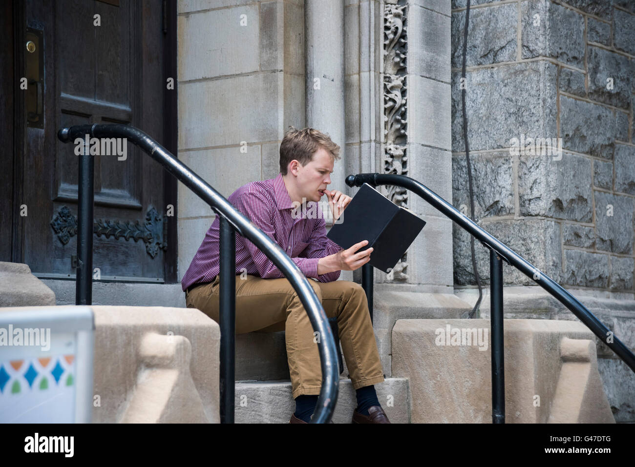 Ein junger Mann sitzt auf der Treppe und Lesebuch, Philadelphia, Pennsylvania, USA Stockfoto